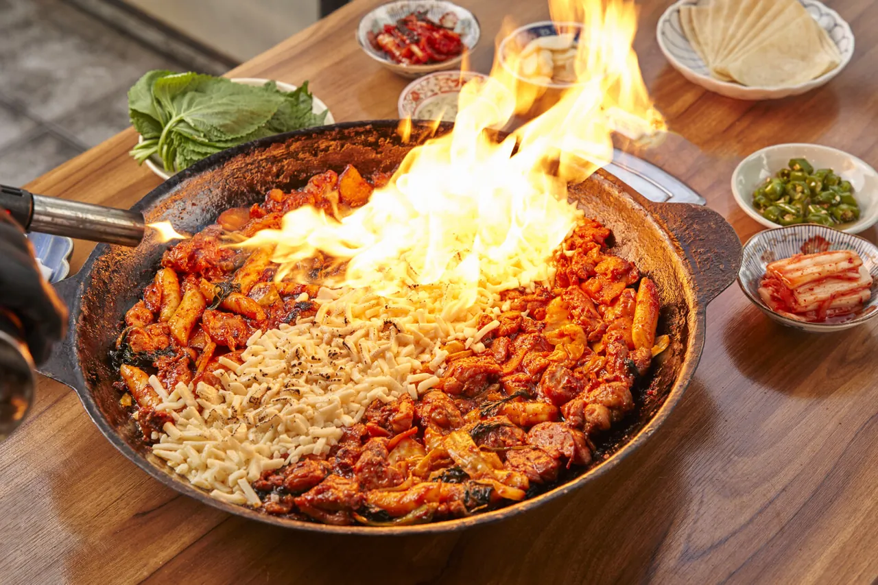 단체 테이블에서 토치로 치즈를 녹이며 불꽃이 올라오는 닭갈비 철판